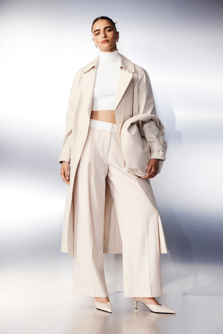 Model in stone double breasted trench coat, pure white crop high neck knit, stone waisted detail pant, stone kitten mule and silver sofia huggie earrings