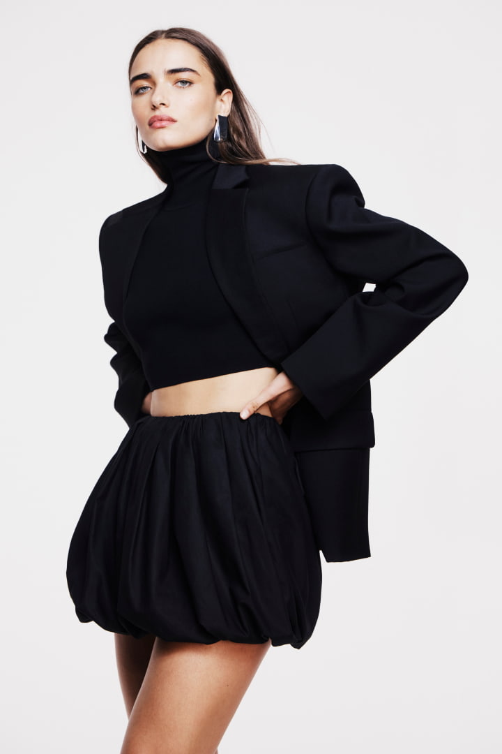 Model in black oversized single breasted blazer, black crop high neck knit and black bubble skirt