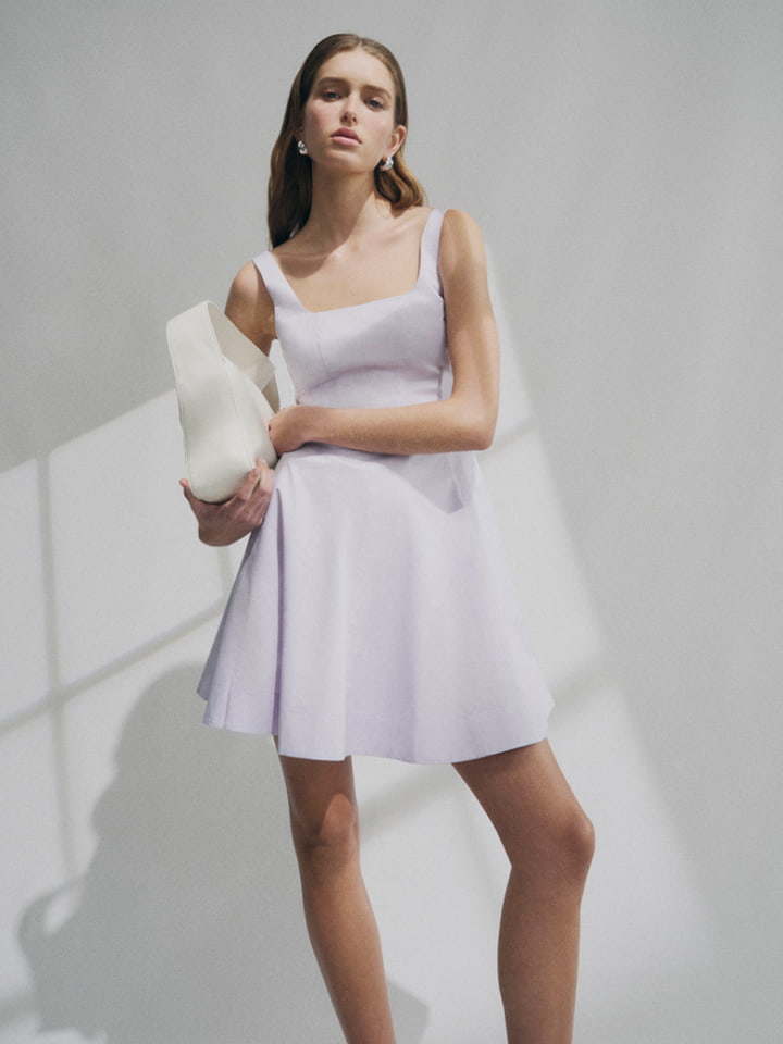 Woman in lilac mini seam detail dress and cream lily shoulder bag